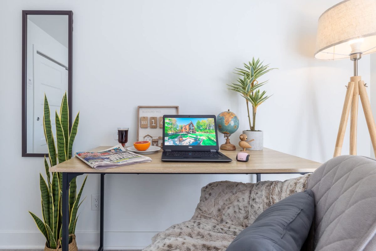 Coin bureau avec portable, globe terrestre et plantes vertes, près d’un divan gris