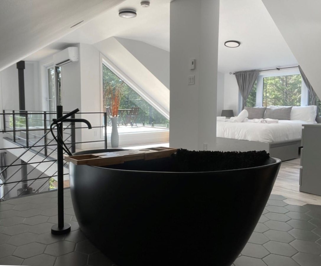 Baignoire autoportante noire à l’étage, plancher de tuiles hexagonales et lit près des fenêtres