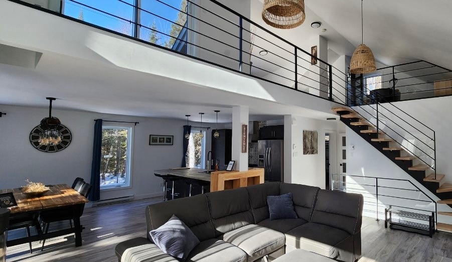 Aire ouverte à double hauteur, mezzanine à garde-corps noir, cuisine avec îlot et escalier