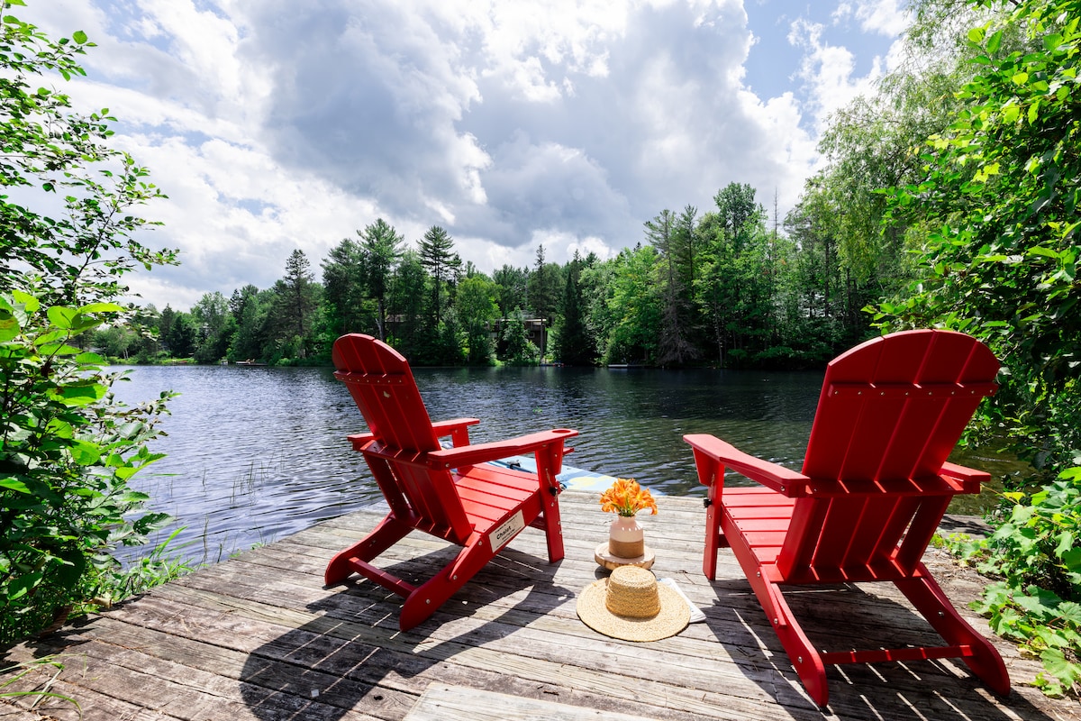 Deux chaises Adirondack rouges sur le quai de bois, face au lac et à la forêt