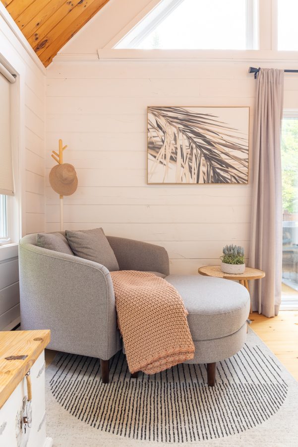 Fauteuil rond gris avec jeté rose tricoté, devant un mur de planches blanches