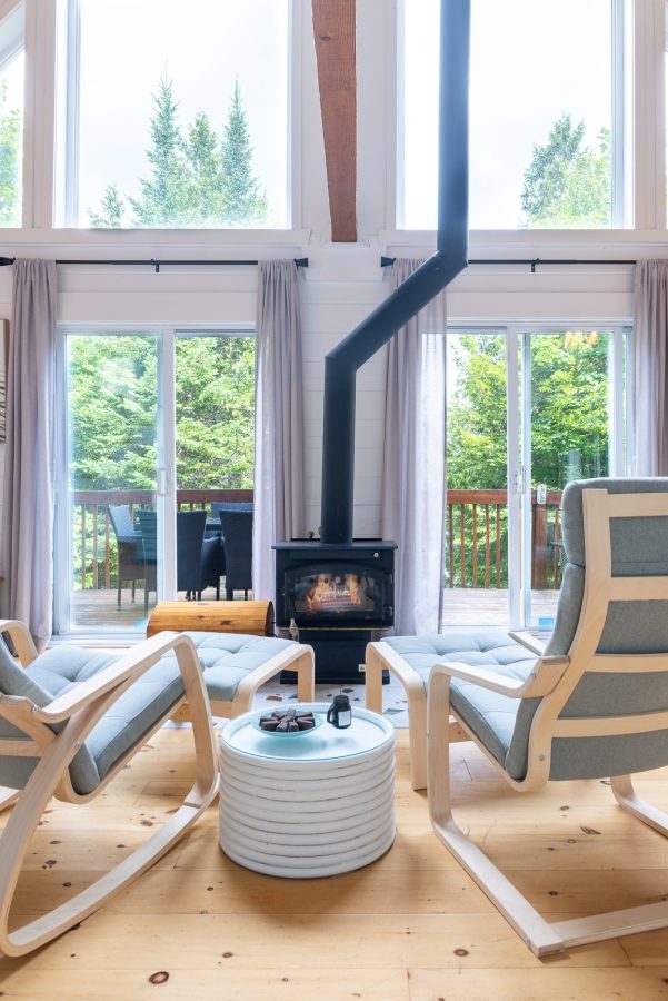 Poêle à bois allumé au salon, fauteuils clairs et portes-fenêtres ouvrant sur la terrasse