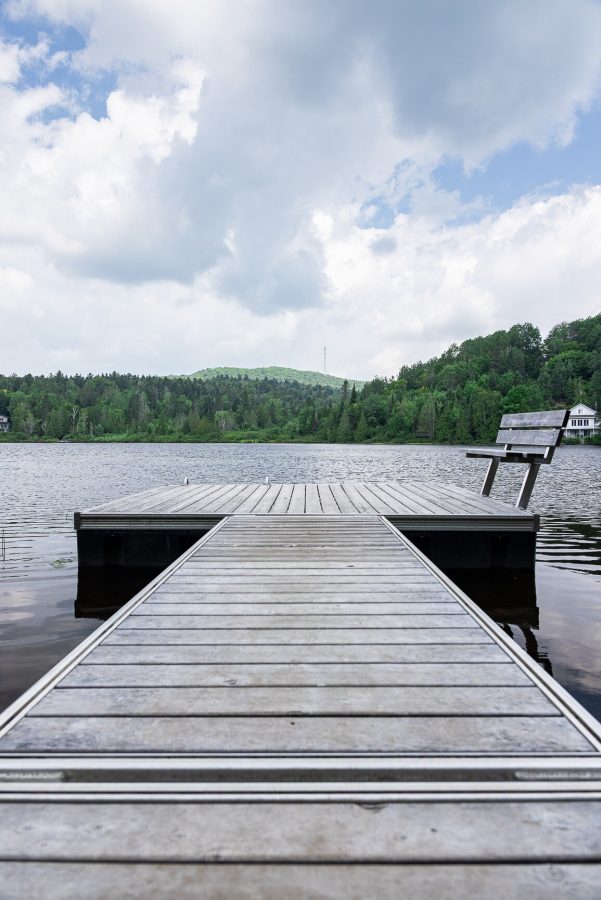 Quai de bois avec un banc au bout, lac tranquille et collines boisées à l’horizon