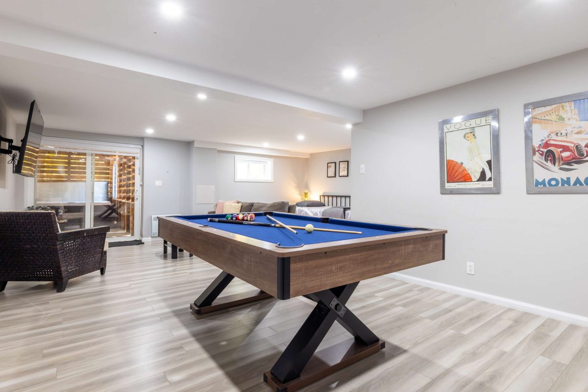 Table de billard bleue au sous-sol, affiches encadrées et coin salon à l’arrière
