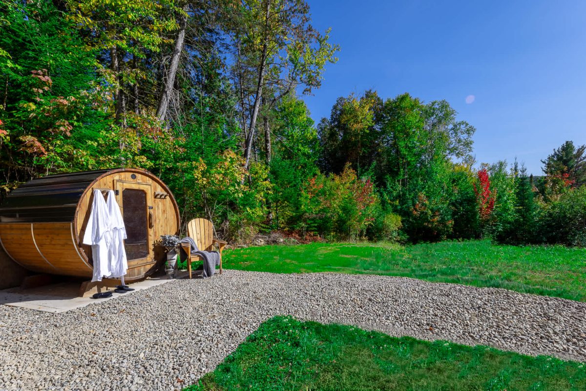 Sauna tonneau de bois au bord de la pelouse, peignoir suspendu et chaise Adirondack