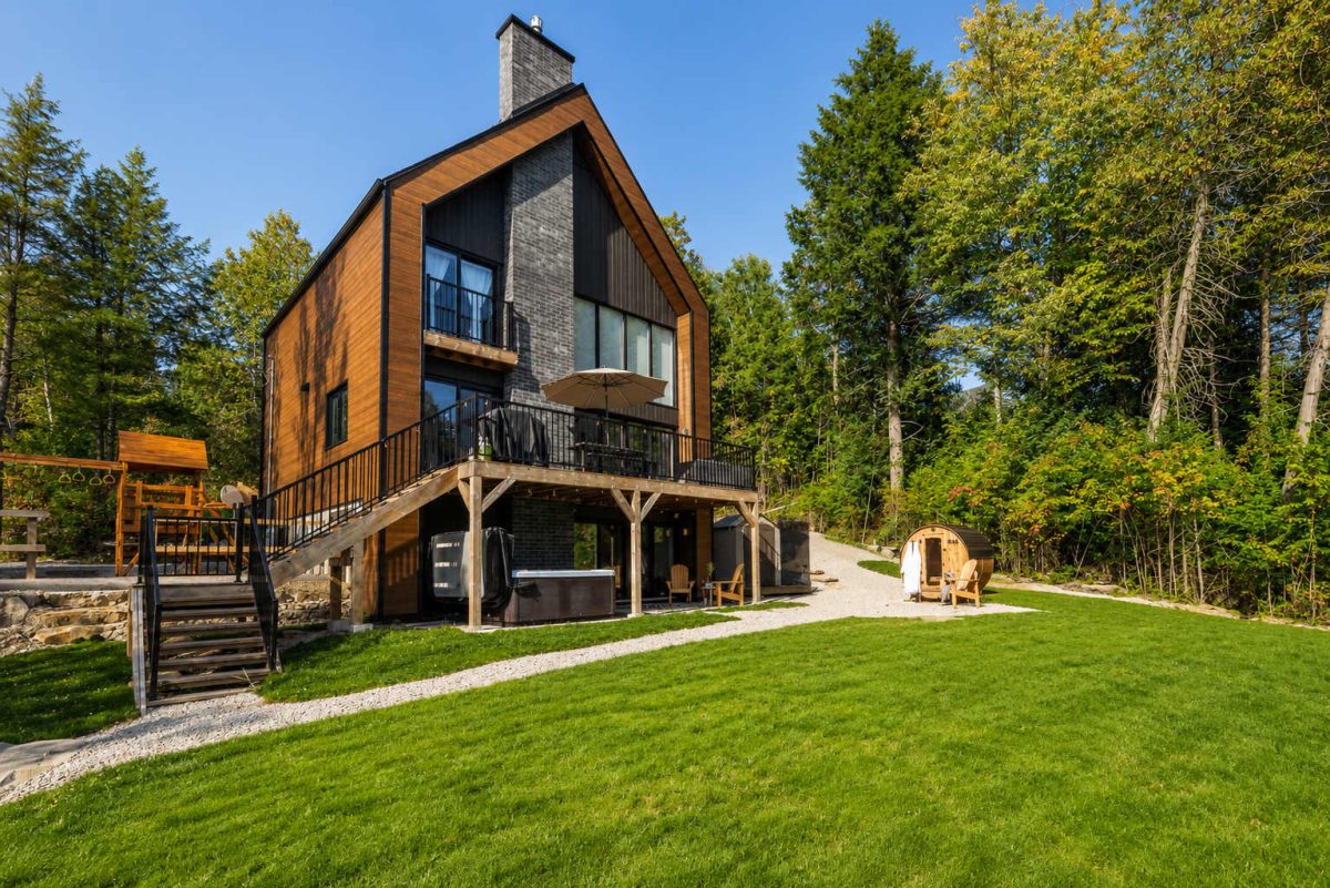 Le Cassiopée, façade de bois et de bardage noir avec balcon, spa sous la terrasse et sauna tonneau
