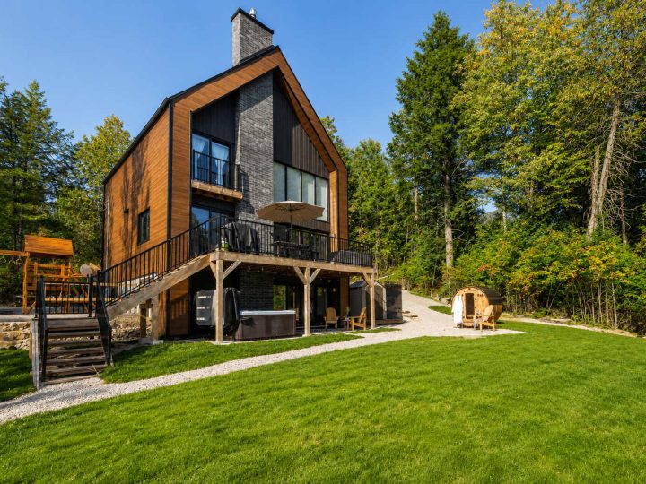 Le Cassiopée, façade de bois et de bardage noir avec balcon, spa sous la terrasse et sauna tonneau