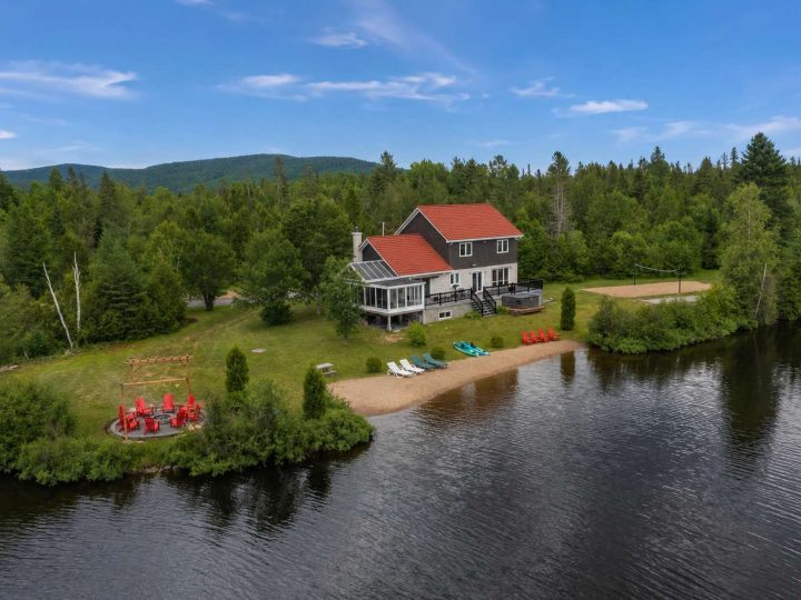 Vue aérienne du chalet Domaine Montanea au bord de l’eau, plage de sable et chaises rouges