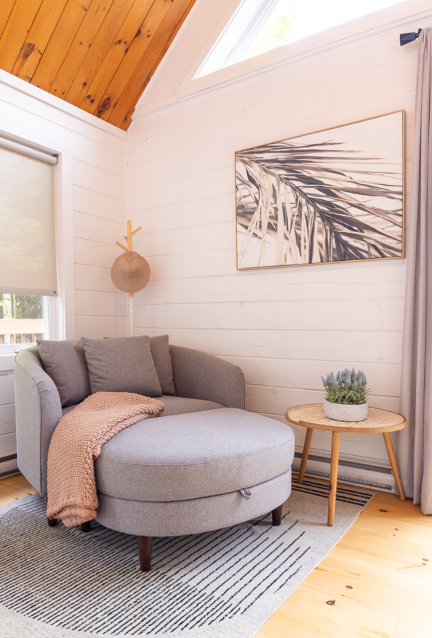 Round grey armchair with a pink knitted throw against a white plank wall, under the gable’s wood ceiling